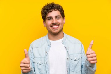 Sarışın adam jest Yaşasın vererek izole sarı duvarın üzerinden