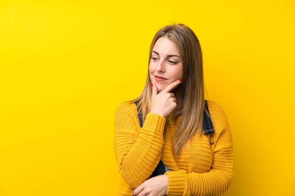 Woman with overalls over isolated yellow wall thinking an idea