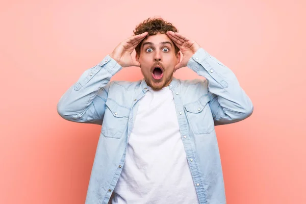 Blonde man over pink wall with surprise and shocked facial expression