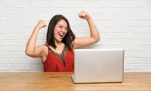 Young Mexican woman with a laptop celebrating a victory