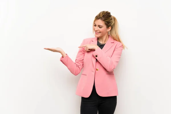 Young blonde woman with pink suit holding copyspace imaginary on the palm to insert an ad