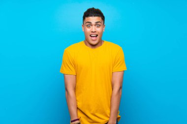 Young man with yellow shirt over isolated blue background with surprise facial expression