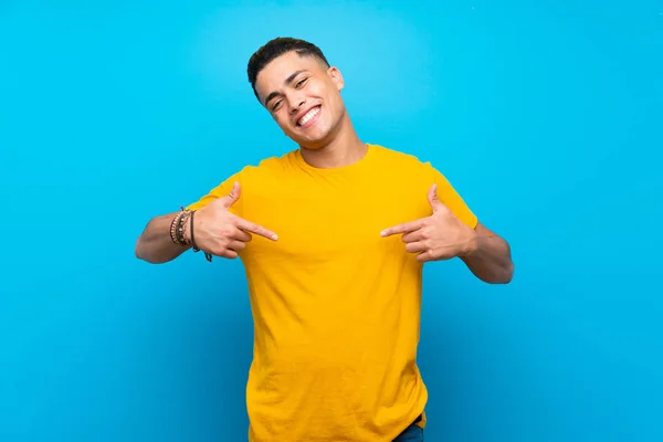 Young man with yellow shirt over isolated blue background proud and self-satisfied