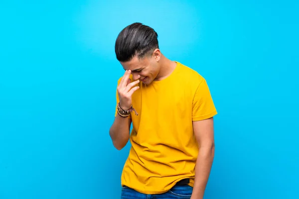 Young man with yellow shirt over isolated blue background smiling a lot