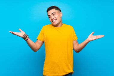Young man with yellow shirt over isolated blue background holding copyspace with two hands