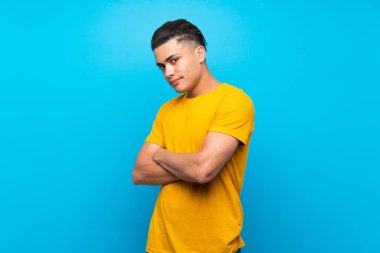Young man with yellow shirt over isolated blue background portrait