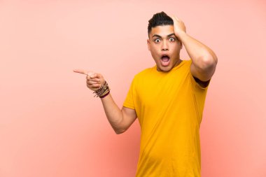 Young man with yellow shirt over isolated pink wall surprised and pointing finger to the side