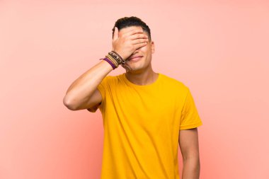 Young man with yellow shirt over isolated pink wall covering eyes by hands