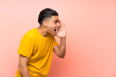 Izole pembe duvar üzerinde sarı gömlekli genç adam ağzı tamamen açık bağırıyor