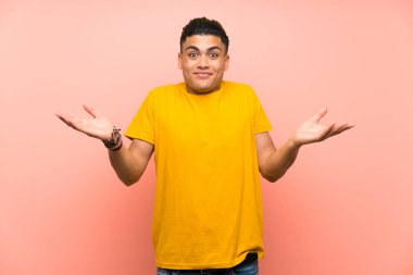 Young man with yellow shirt over isolated pink wall having doubts with confuse face expression