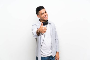 Young man over isolated white wall with earphones with thumbs up because something good has happened