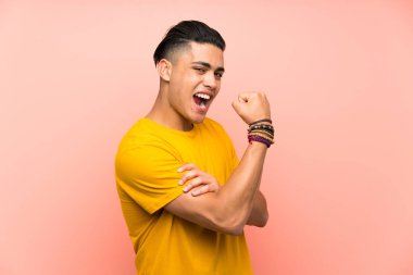 Young man with yellow shirt over isolated pink wall making strong gesture