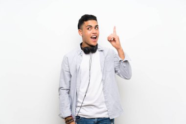 Young man over isolated white wall with earphones intending to realizes the solution while lifting a finger up