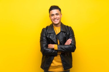 Young man over isolated yellow background keeping the arms crossed in frontal position