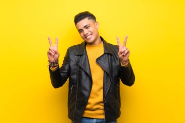 Young man over isolated yellow background showing victory sign with both hands