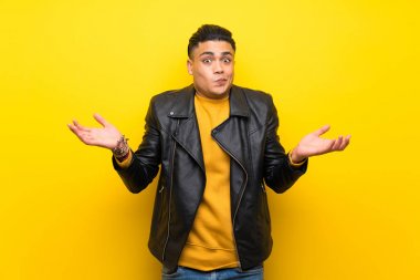 Young man over isolated yellow background having doubts while raising hands
