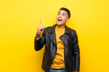 Young man over isolated yellow background pointing up and surprised