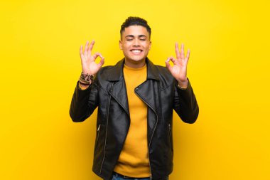 Young man over isolated yellow background in zen pose