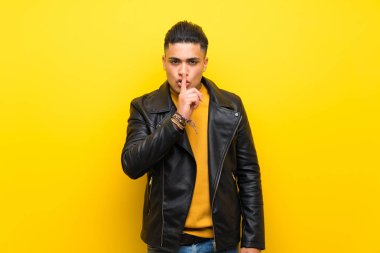 Young man over isolated yellow background showing a sign of silence gesture putting finger in mouth