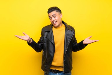 Young man over isolated yellow background holding copyspace with two hands