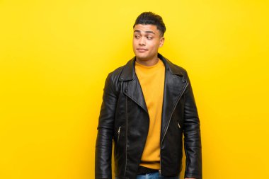Young man over isolated yellow background making doubts gesture looking side