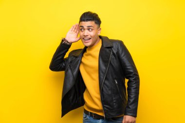 Izole sarı arka plan üzerinde genç adam kulak elini koyarak bir şey dinlerken