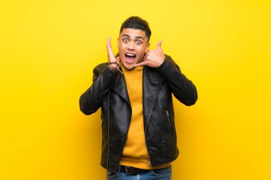 Young man over isolated yellow background making phone gesture and doubting