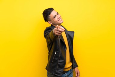 Young man over isolated yellow background points finger at you with a confident expression