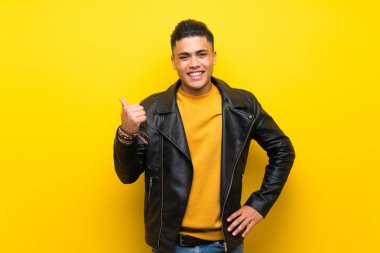 Izole sarı arka plan üzerinde genç adam bir ürün sunmak için yan işaret