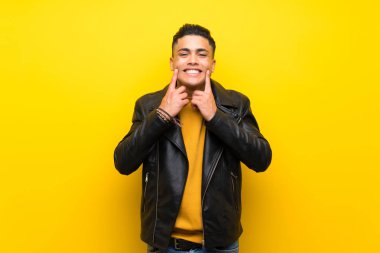 Young man over isolated yellow background smiling with a happy and pleasant expression