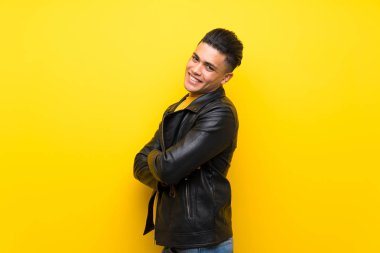 Young man over isolated yellow background with arms crossed and looking forward