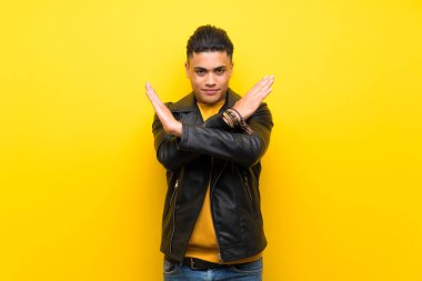 Young man over isolated yellow background making NO gesture