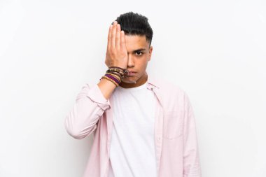 Young man over isolated white wall covering a eye by hand