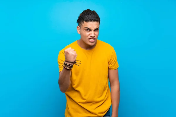 Young man with yellow shirt over isolated blue background with angry gesture