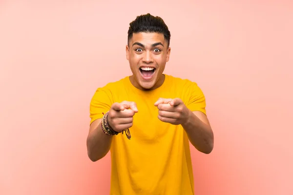 Young man with yellow shirt over isolated pink wall points finger at you