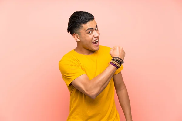 Young man with yellow shirt over isolated pink wall celebrating a victory