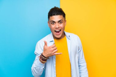 Young man over isolated colorful background making phone gesture