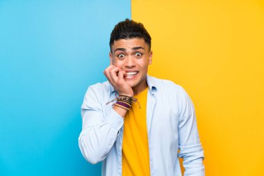 Young man over isolated colorful background nervous and scared
