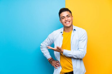 Izole renkli arka plan üzerinde genç adam gelmeye davet için yan ellerini uzatan