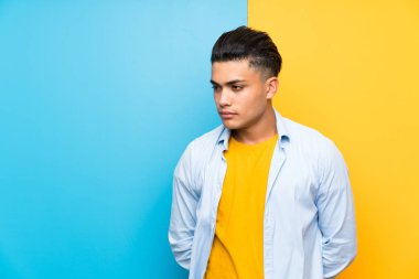 Young man over isolated colorful background looking side