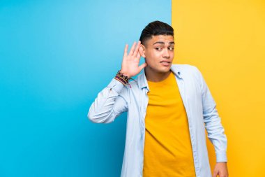 Young man over isolated colorful background listening something