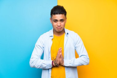 Young man over isolated colorful background pleading
