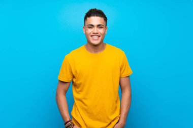 Young man with yellow shirt over isolated blue background laughing