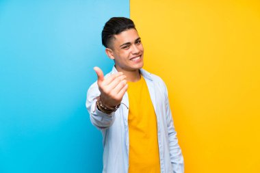 Young man over isolated colorful background inviting to come