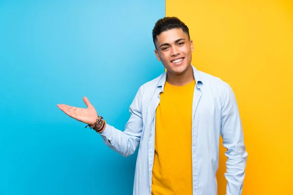 Young Man Isolated Colorful Background Holding Copyspace Imaginary Palm — Stok fotoğraf