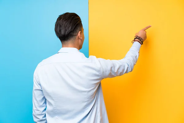 Young Man Isolated Colorful Background Pointing Back Index Finger — Stockfoto