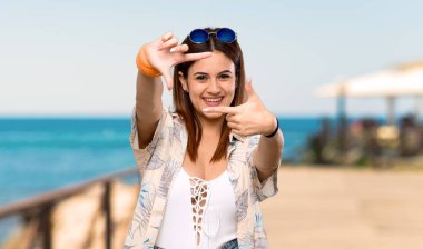 Yaz tatillerinde bikinili genç kadın yüzünü odaklıyor. Sahilde çerçeveleme sembolü