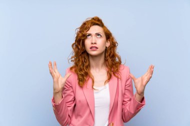 Izole mavi duvar üzerinde takım elbise redhead kadın kötü bir durum tarafından sinirli
