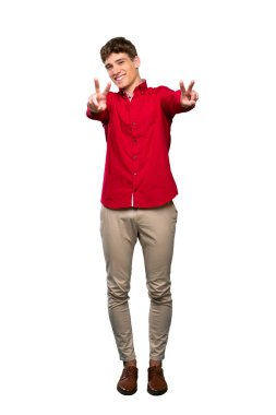 Yakışıklı bir genç adam gülümseyen ve izole beyaz arka plan üzerinde zafer işareti gösteren tam uzunlukta bir çekim