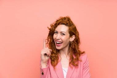İşaret parmağı ile işaret izole pembe duvar üzerinde takım elbise redhead kadın harika bir fikir